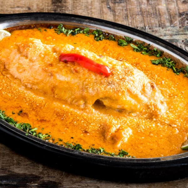 Baked fish in a rich orange sauce, garnished with lime wedges, parsley, and a red pepper.