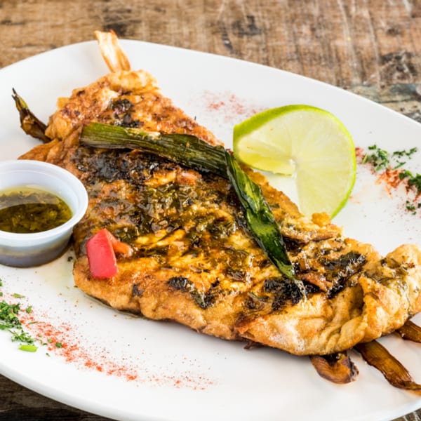 Grilled fish with green onions, lime, and a side of sauce on a white plate.