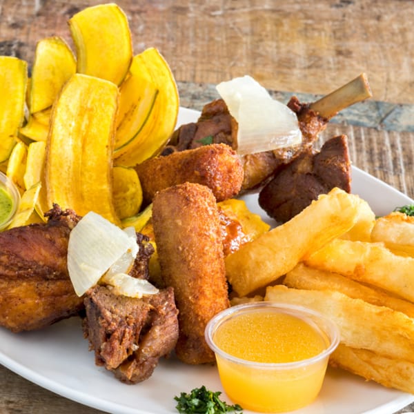 A platter of fried plantains, yuca fries, various meats, and dipping sauces on a wooden table.