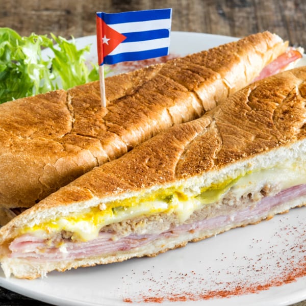 A Cuban sandwich with a Cuban flag toothpick, served with lettuce on a white plate.